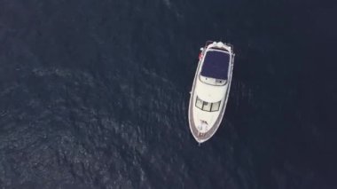 Güneşli bir günde açık denizde yelken açmak için harika bir manzara. Video kaydı. Küçük dalgalanmalar ve su taşıma konseptiyle deniz dokusunda izole edilmiş beyaz bir yelkenli teknesinin havadan görünüşü.