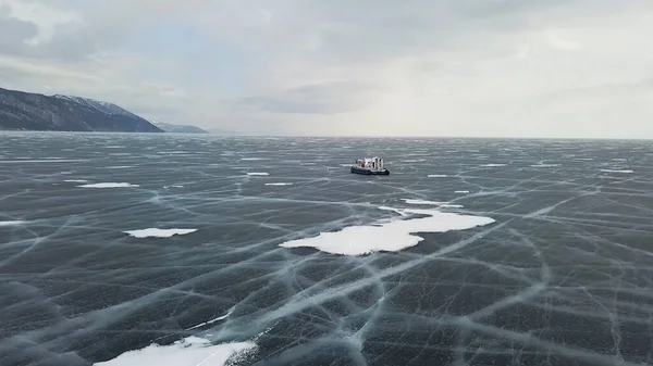 Snow air motion boat goes on big snow field of a frozen lake. Clip. Aerial view of icy surface of the Baikal lake near cliffs of Olkhon Island.