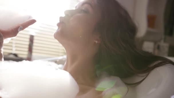 Close upside uitzicht op speelse aantrekkelijke jonge vrouw blazen wit schuim onder het genot van luxe bad. Een video. Begrip sensuele waterverzorging en genot thuis. — Stockvideo