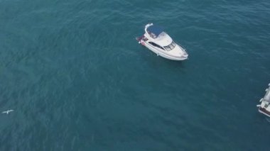 Turkuaz suda yüzen insanların olduğu yatın en üst görüntüsü. Şarjör. Turistler açık denizde tek başlarına yatta rahatlar ve eğlenirler. İnsanlar açık denizde yatın yanında yüzerler.
