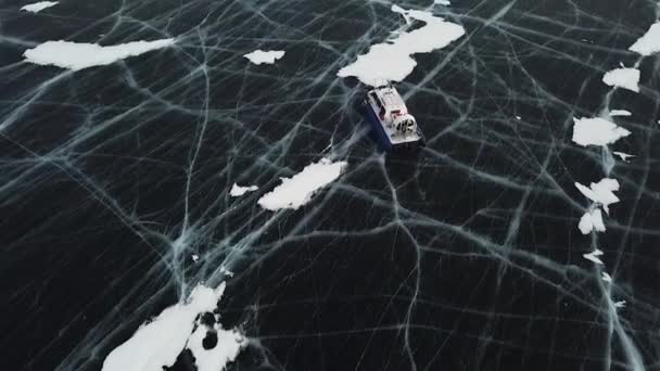 Снегоход идет по большому снежному полю замерзшего озера. Клип. Вид с воздуха на ледяную поверхность озера Байкал возле скал острова Ольхон. — стоковое видео