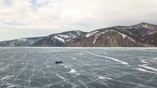 Inverno Baikal Lake com turistas no gelo se divertindo. Clipe. Vista aérea de pessoas que exploram a natureza selvagem do lago congelado no fundo do céu nublado . — Vídeo de Stock