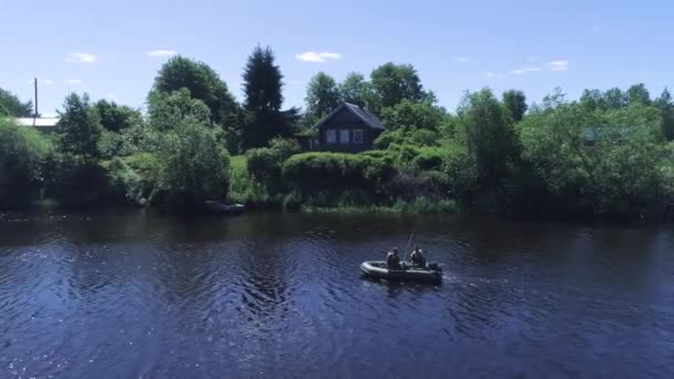 Fishermen in inflatable motor boat float on river. Shot. Top view of fishermen in boat floating on river near green shore with village houses. Summer fishing on river — Stock Video