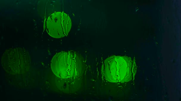 Close-up of window with drops background of blurred lights in dark. Concept. Blurry bright lights shine through wet glass from rain — Stock Video