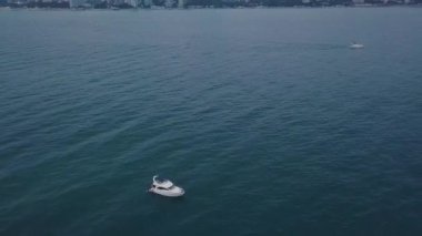 Sahilin arka planında, bulutlu havada şehirli bir yat. Şarjör. Tek başına deniz manzarası, arka plan sahili ve karanlık gökyüzü.