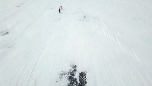 Traîneau à chiens sur un lac gelé en hiver. Clip. Vue aérienne du safari touristique en traîneau huppé à travers une rivière gelée enneigée sur fond de montagnes boisées hivernales et de ciel nuageux lourd. — Video