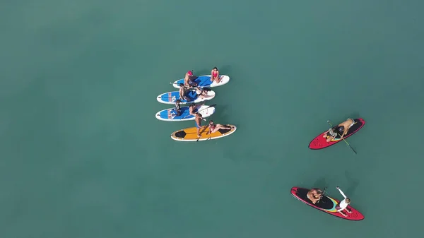 Vista aérea superior de jovens fazendo stand-dup paddleboarding. Vídeo. Conceito de verão e férias, sobrevoando homens e mulheres atraentes sup surf em turquesa fundo de água calma . — Fotografia de Stock