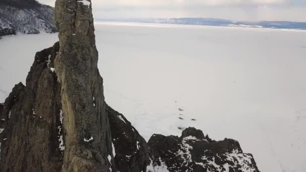 Famoso marco natural na Rússia, Sibéria, Baikal. Clipe. Vista aérea da paisagem de inverno de tirar o fôlego com lago congelado sem fim claro e encostas afiadas de uma colina . — Vídeo de Stock