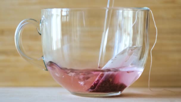Gros plan du brassage du thé rouge dans une tasse transparente. Concept. Le thé devient rouge eau bouillante. Beau thé rouge brassé sur fond en bois — Video
