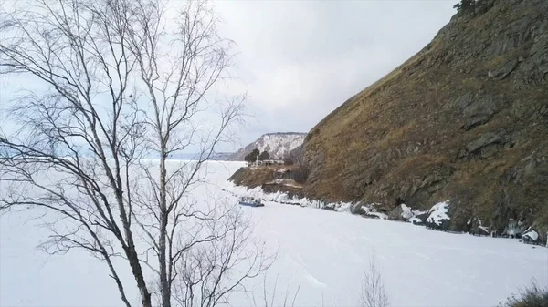 Blick von innen auf einen zugefrorenen See und den Berg. Clip. Luftaufnahme des eisigen Wasserreservoirs mit beweglichen Luftkissenbooten und des Winterberges mit gelbem Gras. — Stockfoto