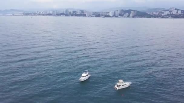 Flygfoto av två segelbåtar i en damm med krusade vattenytan. Videon. Vackra båtar flyter på bakgrunden av avlägsen stad, berg och molnig himmel. — Stockvideo