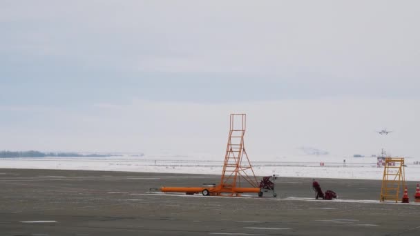 Passengers airplane landing to airport runway on heavy cloudy sky background. Stock footage. Signal cones, ladders standing on the runway on the airport territory. — Stock Video