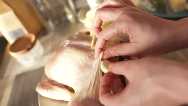 Primer plano de pollo crudo acostado en el plato de la mesa de la cocina. Acción. Concepto de gastronomía, manos femeninas rellenando carcasa de pollo fresco con una cabeza de ajo. — Vídeos de Stock