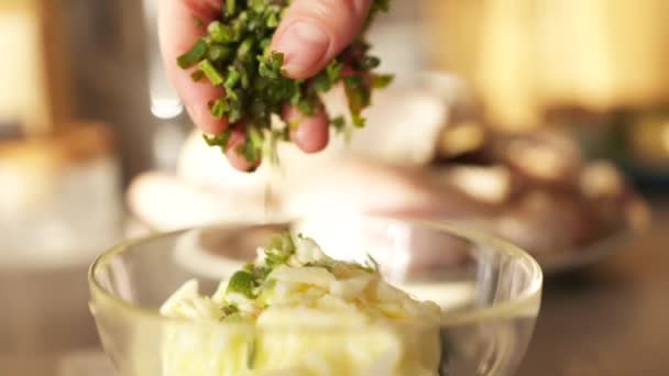 Primer plano de la mano de mujer añadiendo perejil cortado al tazón de cristal con ajo. Acción. Proceso de cocción de alimentos, ajo con vegetación, concepto de dieta de cocina saludable. — Vídeo de stock