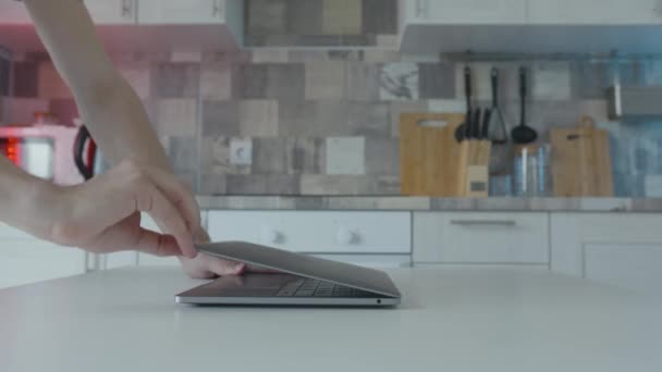 Руки откройте ноутбук на кухне. Начали. Молодой человек открывает ноутбук за кухонным столом. Студент отдыхает дома на ноутбуке. Современный стильный и недорогой ноутбук — стоковое видео