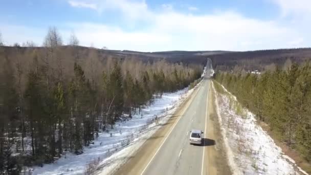 Sorvolando la strada in cemento con veicolo in movimento lungo la pineta. Clip. Veduta aerea del terreno innevato nella foresta e strada di campagna nel tardo autunno con una macchina di guida. — Video Stock