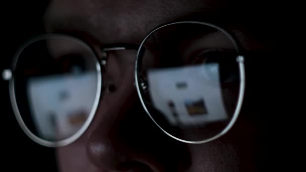 Человек работает в Интернете с отражением монитора внутри очков. Концепция. Крупный план мужского лица в очках с экраном, отраженным в объективах, изолированных на черном фоне. — стоковое видео