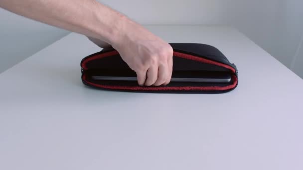 Un homme met un ordinateur portable dans une valise, le referme et enlève la table. L'action. Gros plan de la main masculine plaçant l'ordinateur portable moderne dans les ordures et l'emportant. — Video