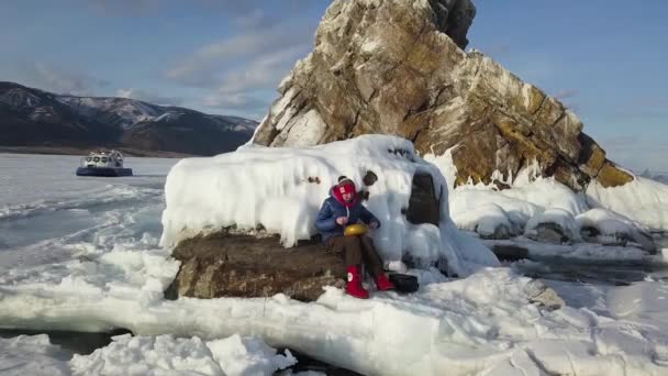 Vue aérienne d'une femme jouant du tambour de langue en acier assise sur un rocher au milieu de la neige et de la glace d'un lac gelé. Clip. Méditation avec tambour de réservoir et bâtons. — Video