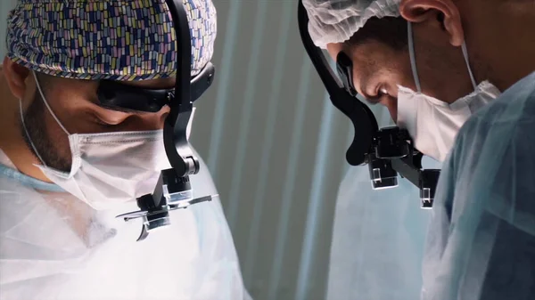 Orvosi csapat végzi a műtétet. Felvétel. Az eljárás során a műtőben távcsövet viselő sebészek arcának közelsége. — Stock Fotó