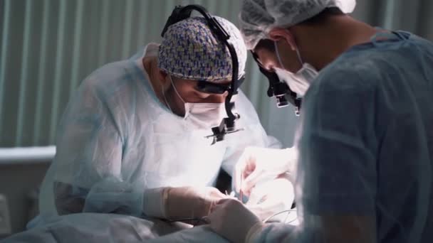 Equipo médico realizando la operación. Acción. Primer plano de las caras de los cirujanos en el trabajo con lupas binoculares en quirófano durante el procedimiento . — Vídeo de stock