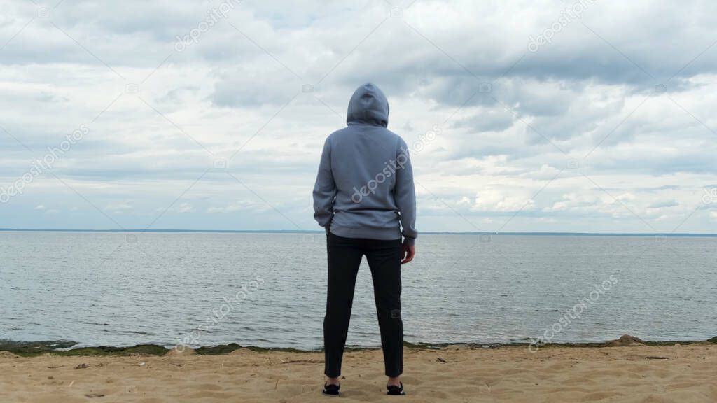 Back view of a male at the Gulf of Finland, Saint Petersburg, Russia. Concept. Rear view of a man in sports clothes standing on the beach and looking far away in the distance.
