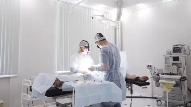 A equipe de médicos realiza a cirurgia enquanto o paciente está sob anestesia. Acção. Vista para dentro da sala de cirurgia com homens cirurgiões e paciente masculino sedado . — Vídeo de Stock