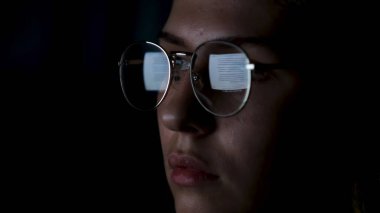 Güzel bir kız internette gözlüklü bir monitörün yansımasıyla çalışıyor. Kavram. Siyah arkaplana izole edilmiş lenslerle yansıtılan gözlüklü kadın yüzünü kapat.