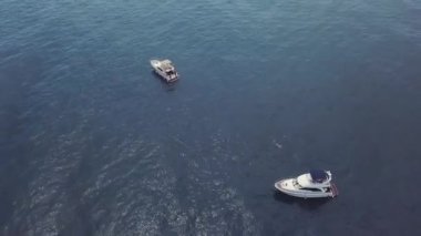 Yelkenlilerin manzarası ve açık denizde yüzen bir adam. Video kaydı. Sonsuz ufuktaki derin mavi denizde iki beyaz yatın inanılmaz hava manzarası..