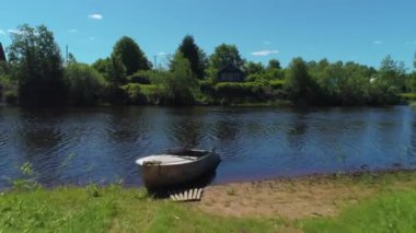 Gölde eski ahşap bir ev ve teknesi olan bir kır manzarası. Vuruldu. Yeşil ağaçlar ve çayırlarla dolu, ekolojik bir yerde yaşayan parlak bir yaz günü..