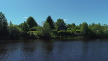 Kırsal kesimdeki bir nehrin kıyısındaki eski ahşap ev. Vuruldu. Ormanın içinde küçük sakin bir nehir ve açık gökyüzü arka planında bir köy evi..
