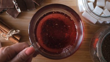 Kırmızı karkade çayı demleme işlemi, üst manzarayı kapatın. Kavram. Taze demlenmiş meyve çayı, çaydanlıktan dökülen sıcak su, ahşap zemin üzerinde cam bir fincana dökülüyor..