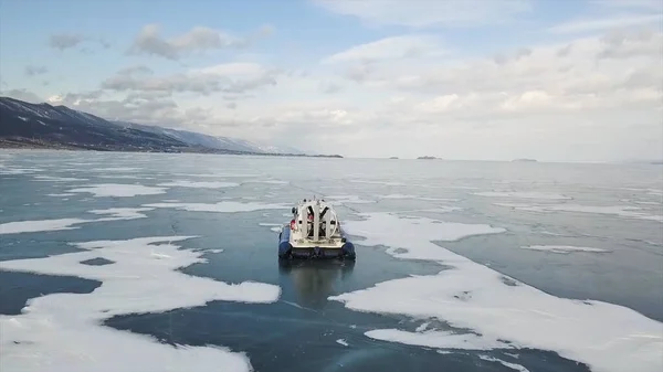 冬にシベリアのバイカル湖にゴム製の空気クッションと車の空中ビュー。クリップ。森林に覆われた山々や青空を背景に、氷や雪の上を速く滑るキボスの後部ビュー. — ストック写真