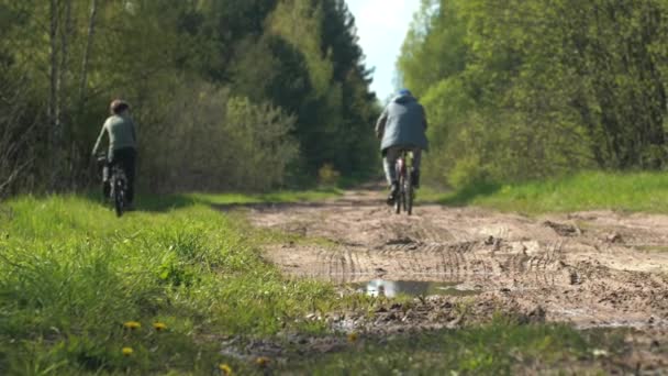 Zadní pohled na otce a jeho syna na kole na venkovské silnici ve vesnici. Pohyb. Muž a chlapec se baví, sportují spolu poblíž zeleného lesa. — Stock video