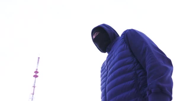 Concept of crime, thief in dark clothes on bright sky background. Action. Suspicious hooded male figure wearing balaclava to hide his face standing and looking around.