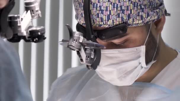 Dwóch chirurgów pracujących w sali operacyjnej. Akcja. Dwóch lekarzy noszących jałowy mundur i lornetkę podczas wykonywania zabiegu chirurgicznego, koncepcji opieki zdrowotnej i medycyny. — Wideo stockowe