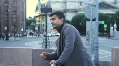 Genç adam şehir merkezindeki caddede buluşmak için bekliyor. Medya. Çekici adam, yoğun bir caddenin arka planında kız arkadaşını bekliyor.