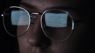 Kadınlar dizüstü bilgisayar kullanır ve geceleri makale okurlar. Kavram. Büyük gözlüklü genç bir kadının yüzünü ve siyah arka planda izole edilmiş lenslerdeki yansımasını kapat..