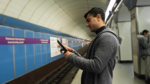 Adam metroda tablet kullanıyor. Medya. Genç adam metroda tren beklerken tablet kullanır. Genç adam elinde tabletle metro trenini bekliyor. — Stok video