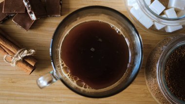 Yakın plan şeker küpleri kahveye eklenir. Kavram. Tarçın arkaplanda ev yapımı kahve ve ahşap masada tatlılar.