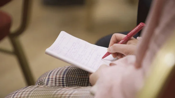 Primo piano di una donna che prende appunti nel quaderno della conferenza. Art. Donna scrive rapidamente in notebook in grembo durante il discorso altoparlanti a coaching — Foto Stock