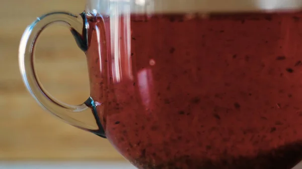 Nahaufnahme von rotem Tee, der in einem durchsichtigen Becher aufgebrüht wird. Konzept. Tee färbt kochendes Wasser rot. Schöner roter Tee gebrüht auf Holzgrund — Stockfoto