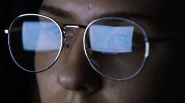 Karanlıkta bilgisayara bakan gözlüklü bir kadın. Kavram. Gözlüklü kadın bilgisayardaki yazıları okurken gözlerini süzüyor.