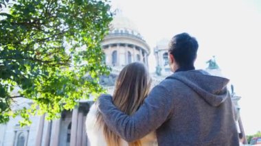 Birkaç kucaklaşma ve Katedral 'e bakma. Kavram. Tatilde olan güzel bir çift tarihi şehir manzarasına bakıyor. Arka planda kadın ve erkeğin yeşil ağaç ve güneş altındaki katedralin arka görüntüsü
