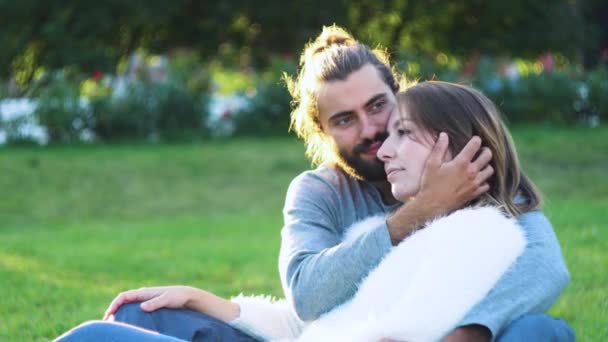 Piękna para przytulająca się na trawie w parku. Koncepcja. Młody mężczyzna i kobieta czule objąć siedząc na zielonej trawie w parku. Kochankowie relaksują się na trawie — Wideo stockowe