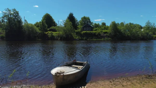 Landskap med gammalt trähus på sjön med båt. Skjuten. Ljus sommardag på byn med gröna träd och äng, boende på ekologisk plats. — Stockfoto