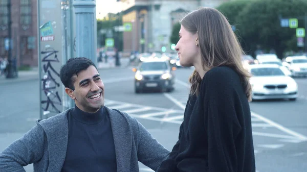 Pareja hablando de pie en la calle ocupada. Medios. Joven hombre y mujer hablan sobre el fondo borroso del tráfico nocturno en la intersección —  Fotos de Stock