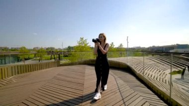 Parkta kamera izleme platformu olan güzel bir kadın. Başla. Kadın, şehir parkındaki modern gözlem güvertesinden kamera ile fotoğraf çekiyor.