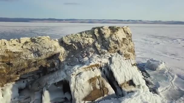 Vista aérea de un enorme lago congelado cubierto de nieve con un acantilado que se eleva a través del hielo. Clip. Paisaje invernal del embalse natural de agua y una colina pedregosa. — Vídeos de Stock