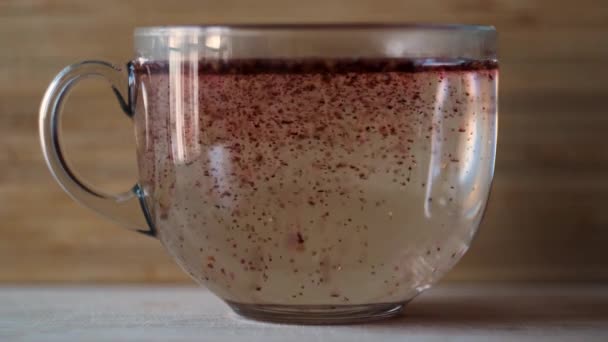 Faire du thé hibiscus avec de l'eau bouillante dans une grande tasse en verre sur fond de mur en bois. Concept. Gros plan de thé rouge aux fruits dans une tasse en verre transparent debout sur une surface de table plane. — Video